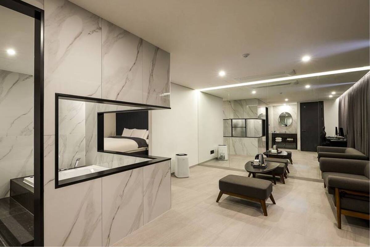 A modern hotel room with a marble wall, a large mirror, a bed, a seating area with a coffee table, and a TV.