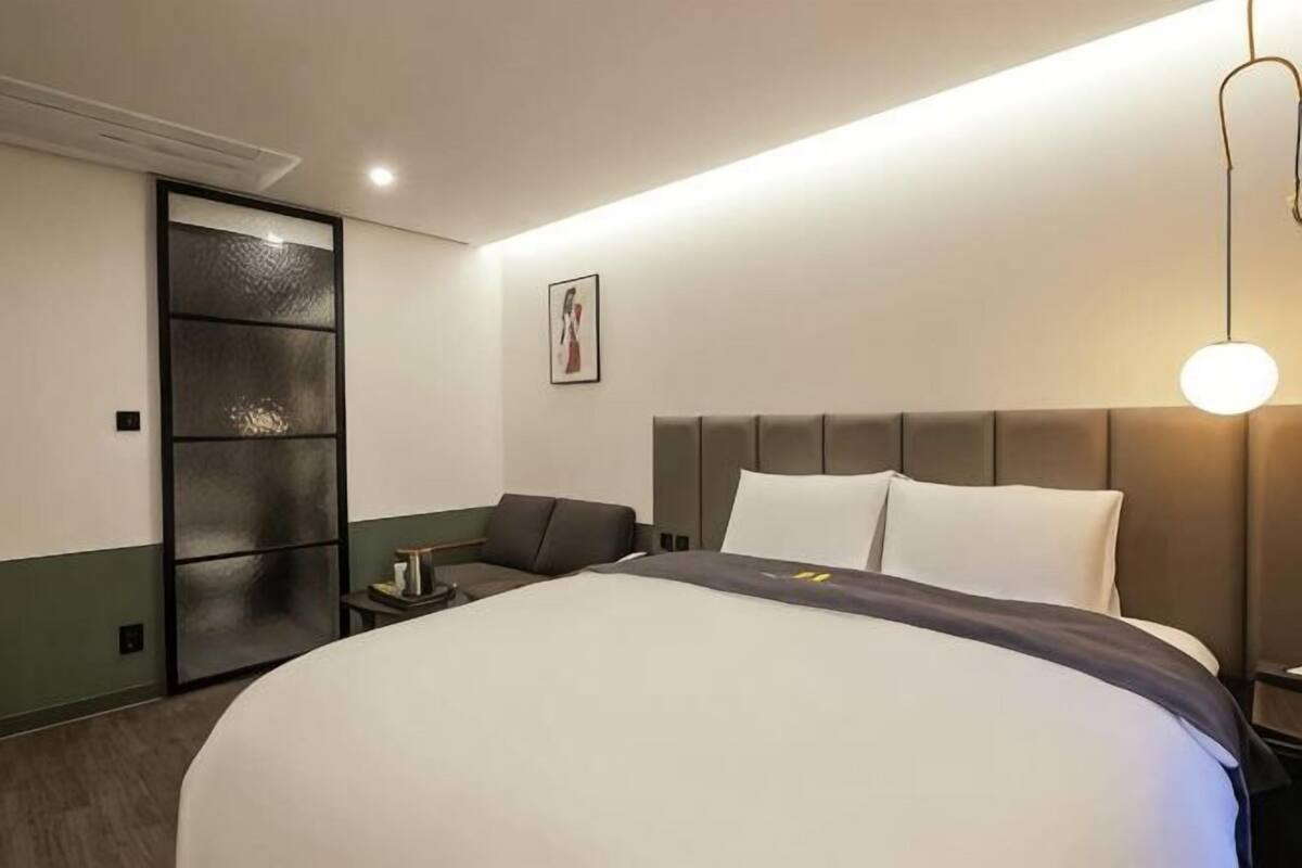 A hotel room with a large bed, a nightstand, a lamp, and a sliding door.