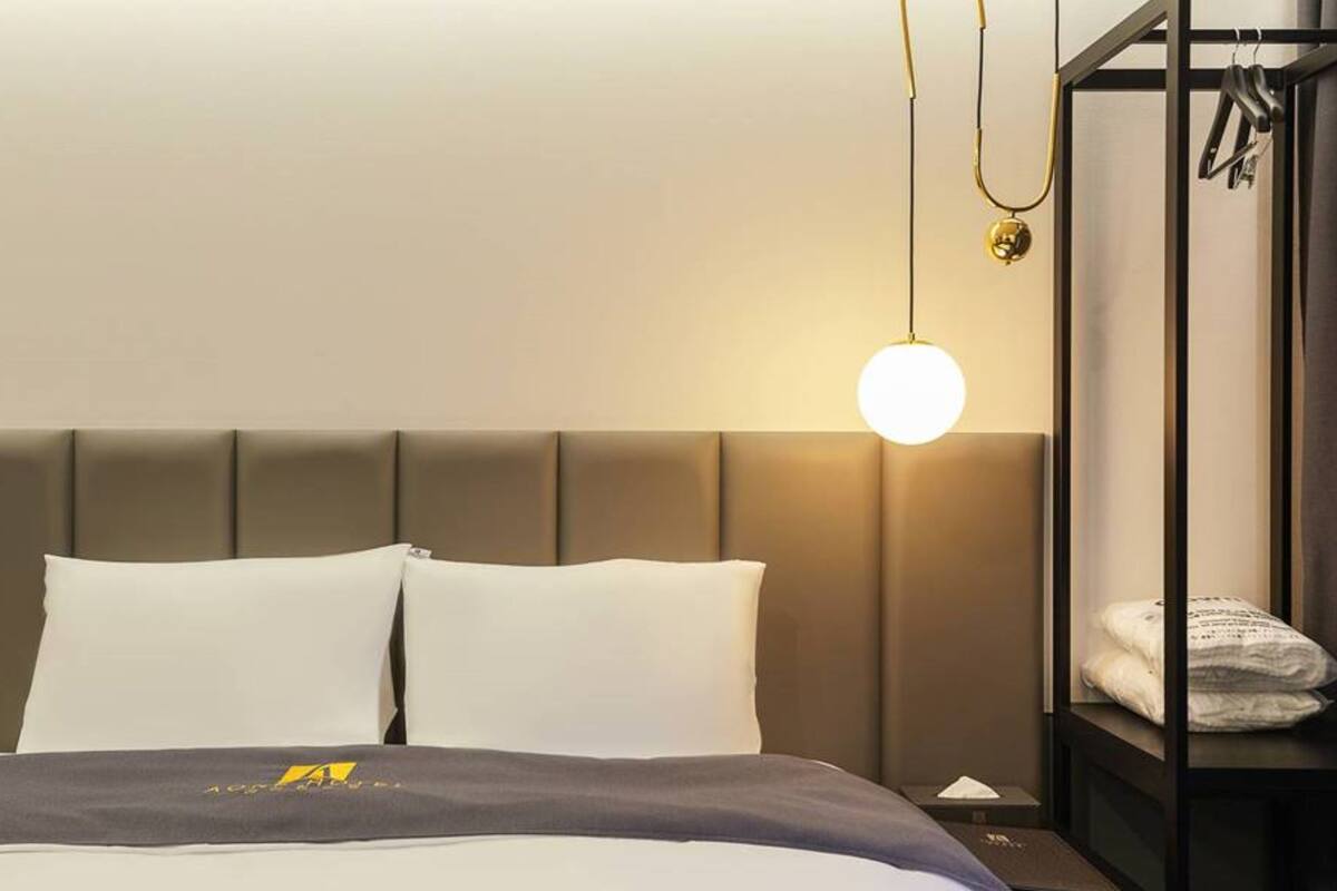 A hotel room with a large bed, a headboard, a bedside table, and a hanging light fixture.