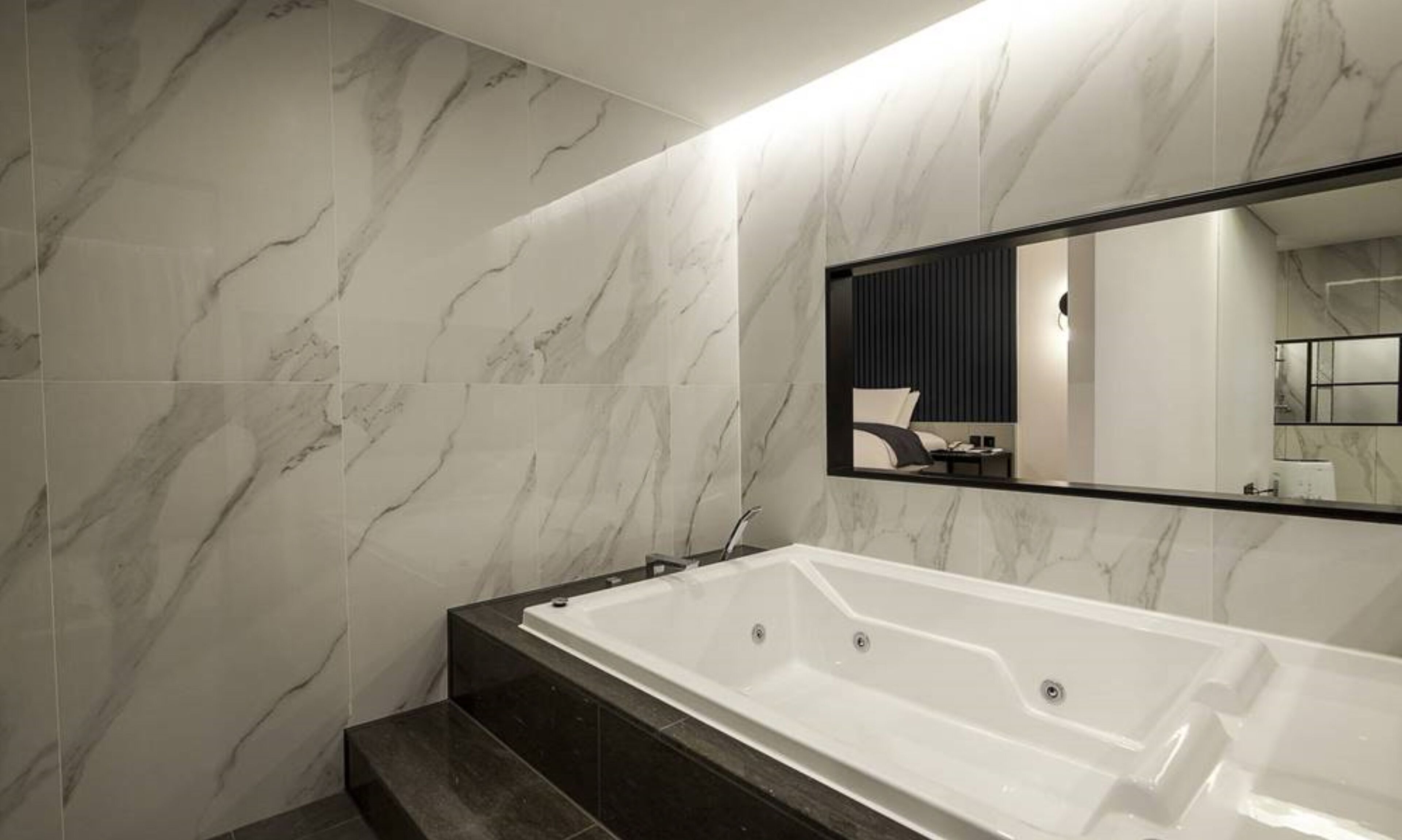 A modern bathroom with a large bathtub, dark marble tiles, and a large mirror.