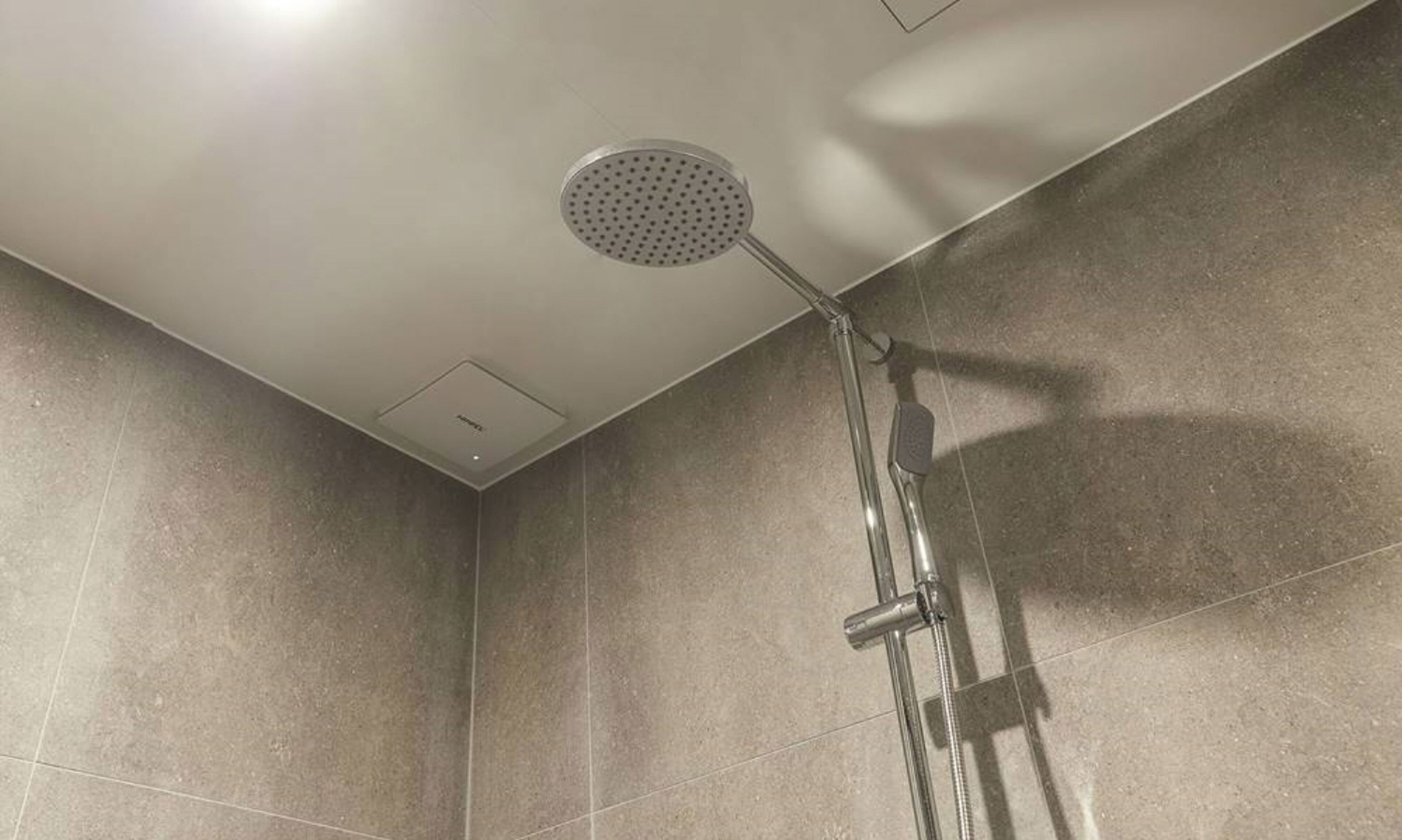 Una ducha con cabezal de ducha manual y grifo empotrado en un baño con azulejos.
