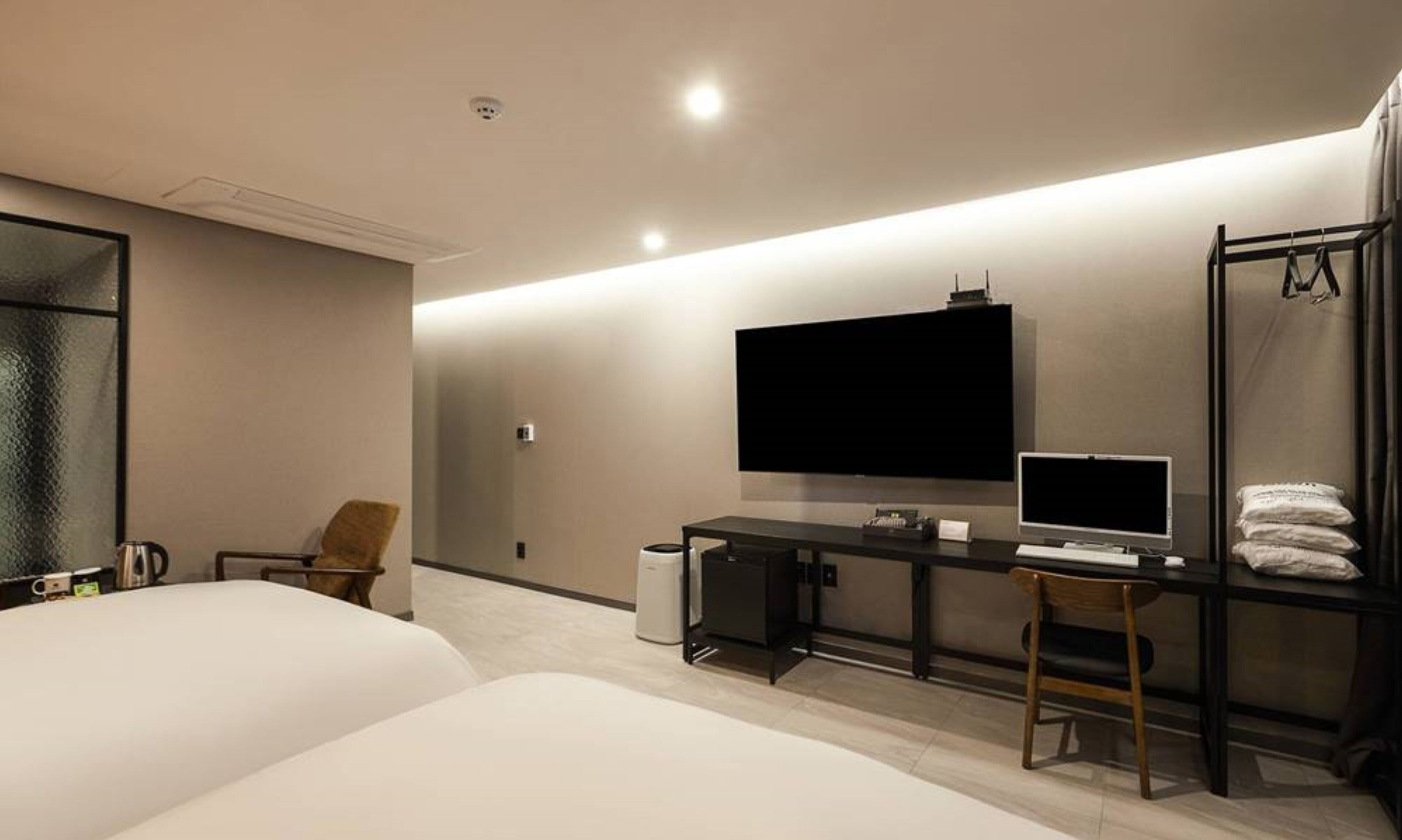 A modern hotel room with a large bed, a desk with a computer, a TV, and a seating area with a chair.