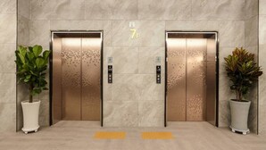 Two elevator doors with a digital display indicating floor 7F, flanked by potted plants. - Namyangju Aone Hotel (Namyangju)