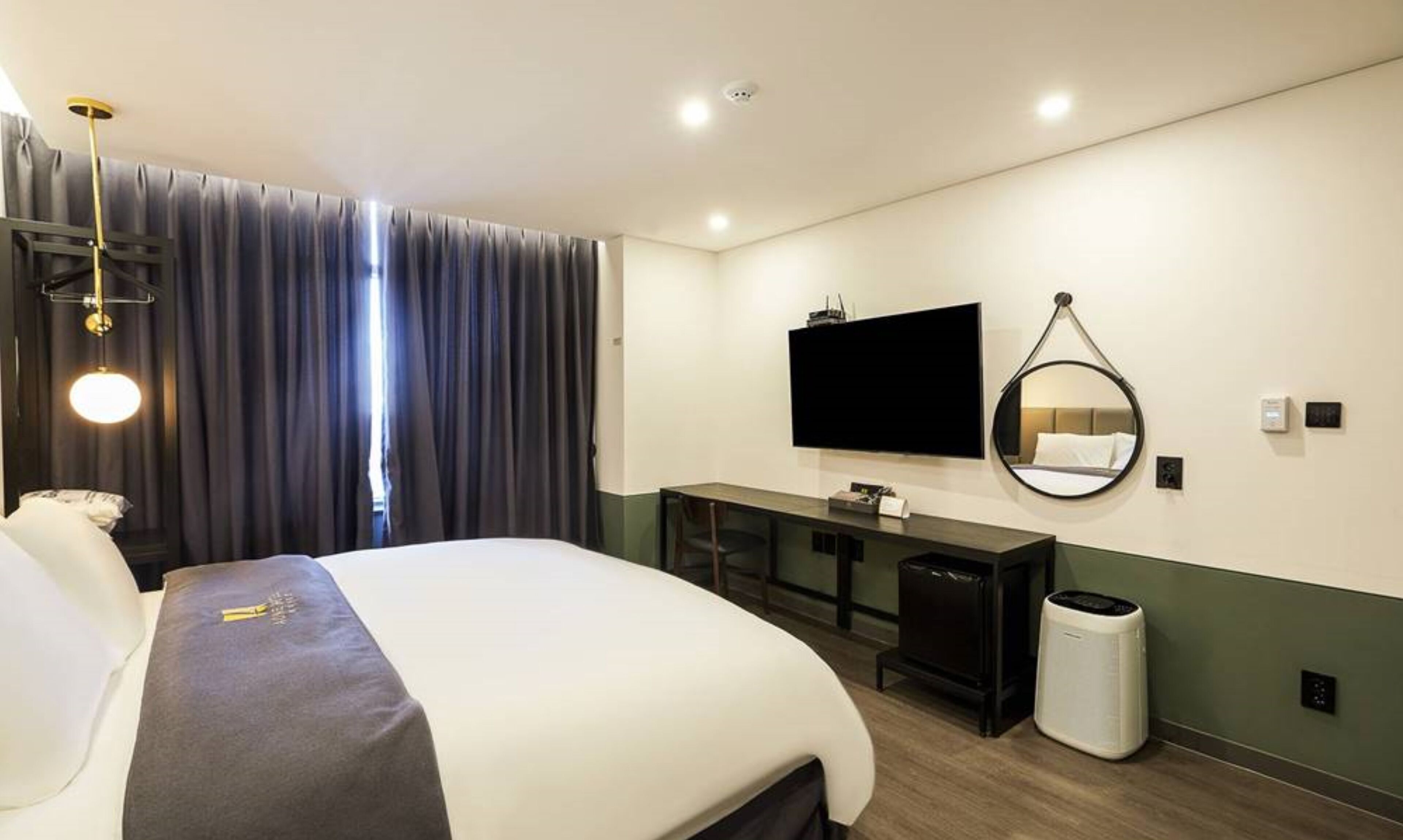 Una habitación de hotel con una cama, un escritorio, un televisor, un espejo y un cesto de basura.