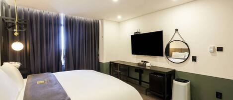 Una habitación de hotel con una cama, un escritorio, un televisor, un espejo y un cesto de basura.