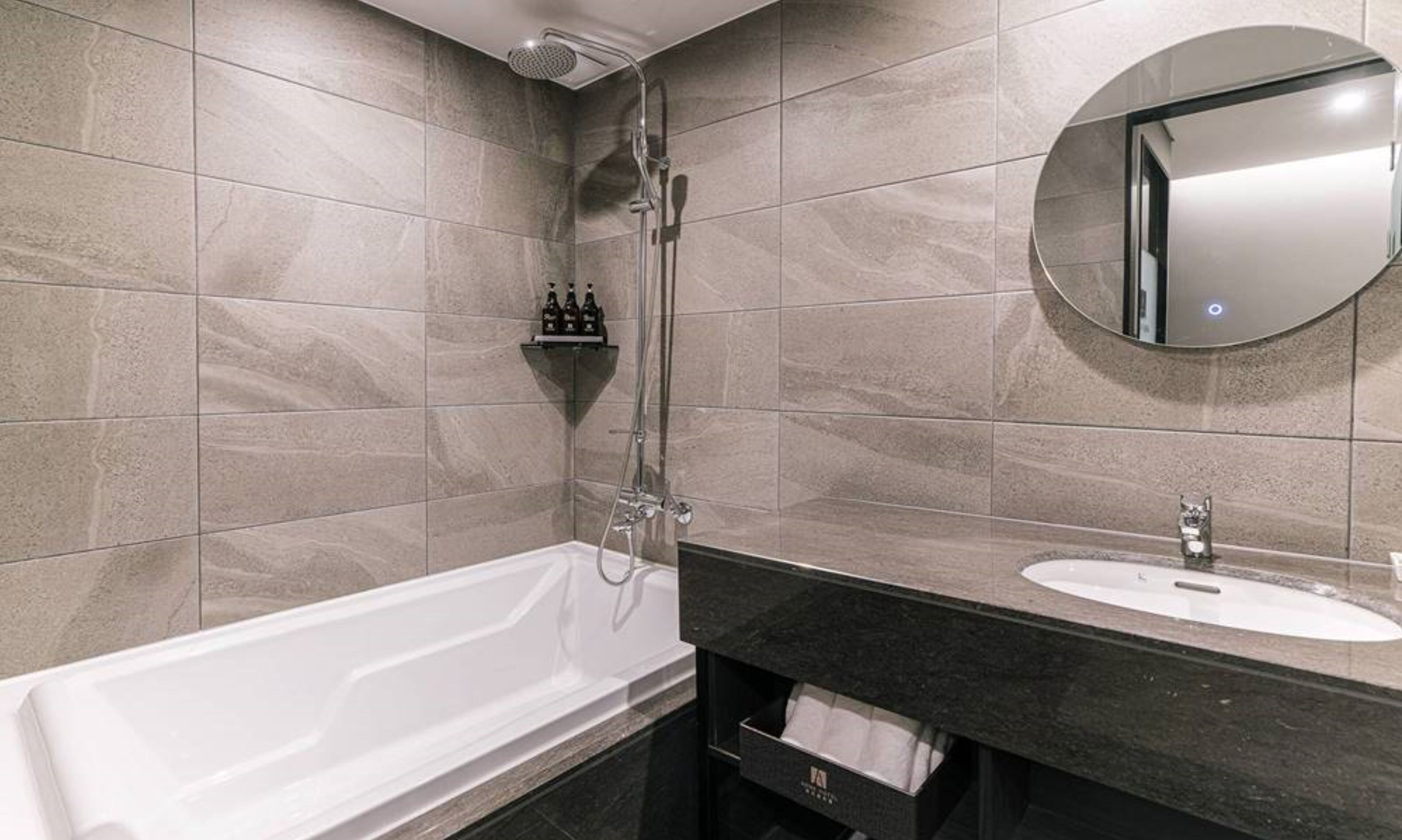 A modern bathroom with a bathtub, a round mirror, and a sink.