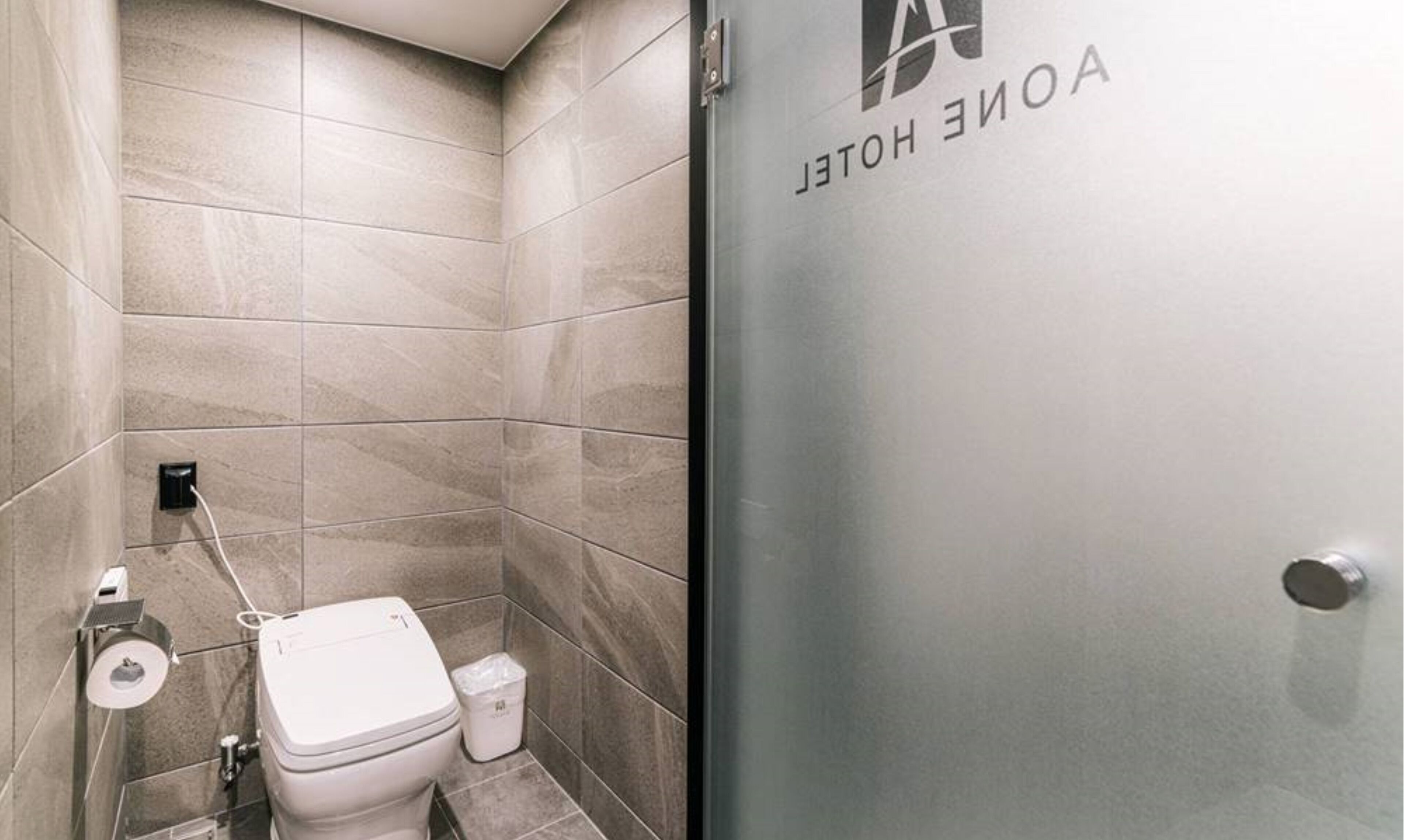 Une salle de bain moderne équipée de toilettes, d’une poubelle et d’un lavabo fixé au mur.