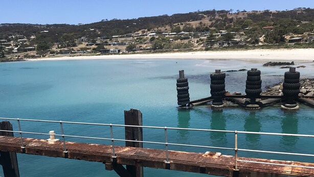 A coastal view with a wooden pier, clear blue water, and a sandy beach in the background. - Fresh, relaxed 2 bedroom apartment, only 1.9kms from the beach, close to shops (Kingscote)