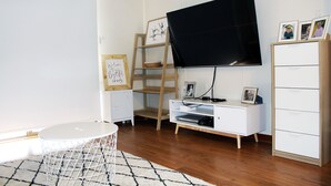 A modern living room with a flat-screen TV mounted on the wall, a white entertainment unit, a wooden ladder shelf, and a white cabinet with drawers. - Fresh, relaxed 2 bedroom apartment, only 1.9kms from the beach, close to shops (Kingscote)