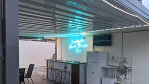 An outdoor bar area with a neon sign, bar stools, a refrigerator, and a sink. - Fresh, relaxed 2 bedroom apartment, only 1.9kms from the beach, close to shops (Kingscote)