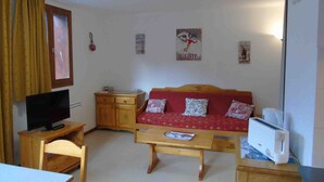 A small, cozy living room with a red sofa, wooden furniture, a television, and a toaster. - Cozy apartment in Valfréjus, near lifts (Modane)