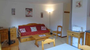 A small, cozy room with a red sofa, wooden furniture, a desk with a printer, and a wall-mounted lamp. - Cozy apartment in Valfréjus, near lifts (Modane)