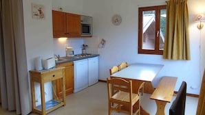 A compact kitchen with wooden cabinets, a microwave, a sink, and a dining area with a table and chairs. - Cozy apartment in Valfréjus, near lifts (Modane)