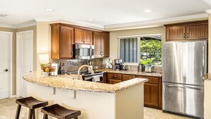 Une cuisine moderne avec des meubles en bois, un réfrigérateur en acier inoxydable, un plan de travail en granit et une fenêtre donnant sur un jardin.
