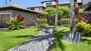 Il s'agit d'une propriété résidentielle dotée d'une allée pavée menant à un garage, et entourée de pelouses bien entretenues et de plantes tropicales.