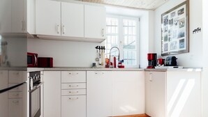 Moderni keittiö, jossa on valkoiset kaapit, sisäänrakennettu uuni ja ikkuna, josta tulee luonnonvaloa.