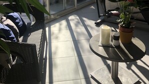 Eine sonnendurchflutete Terrasse mit Glastür zu einem Whirlpool, einem Tisch mit Kerzen und einem Blumentopf.
