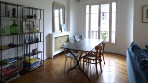 Une pièce comprenant une table à manger, des chaises, une bibliothèque et une fenêtre donnant sur des immeubles.