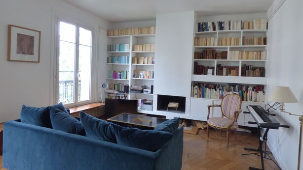 Un salon avec un canapé bleu, une bibliothèque, un fauteuil et un piano.