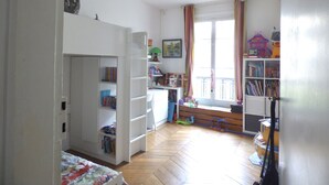 Une pièce avec un parquet en bois disposé en motif à chevrons, des murs blancs et une fenêtre avec des rideaux.