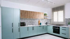 Una cocina moderna con gabinetes verde azulado, un estante superior de madera, salpicadero con diseño y un horno empotrado.
