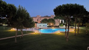 A swimming pool surrounded by a fenced area, with trees and a building in the background. - IN THE QUIET AREA OF NOVO SANCTI PETRI (Chiclana de la Frontera)