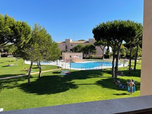 Une piscine entourée de pelouse, d’arbres et d’un bâtiment en arrière-plan.
