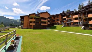 Un hotel de varios pisos con balcones, un patio con césped y vistas a la montaña.
