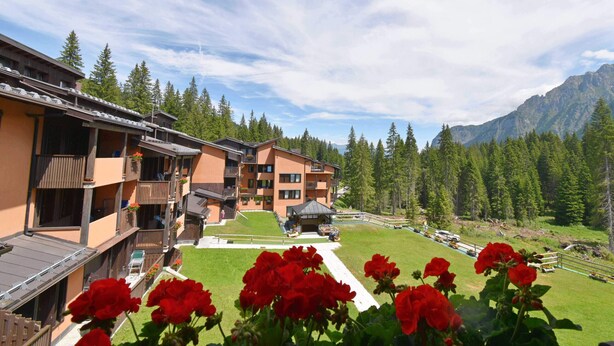 Un hotel con varios balcones, césped y montañas al fondo.