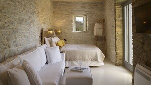 Habitació amb paret de pedra, bigues de fusta, llit, sofà, finestra i televisió.