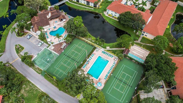 Vista aérea de una propiedad con cancha de tenis, piscina y un pequeño muelle junto al agua.