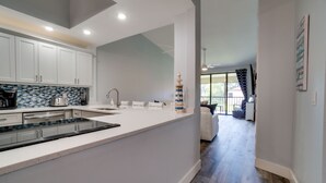 A modern kitchen with white cabinets, a tiled backsplash, and a central island. - Near IMG - Shorewalk Unit 202 by SeaBreeze Vacation (Bradenton)