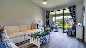 A modern living room with a sofa, coffee table, and a view through large sliding glass doors to an outdoor area.