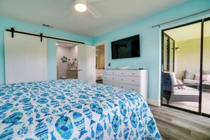 A bedroom with a bed, a dresser, a television, and a sliding glass door leading to a balcony.
