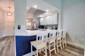 A modern kitchen with white cabinets, a blue accent wall, and a dining area with white chairs.