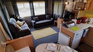 A compact living space with a sofa, dining table set for four, a kitchenette, and a television. - 2-bed Caravan at Billing Aquadrome Northampton (Northampton)