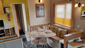 A compact kitchen with a dining area, a sofa, and a small table set for two. - 2-bed Caravan at Billing Aquadrome Northampton (Northampton)