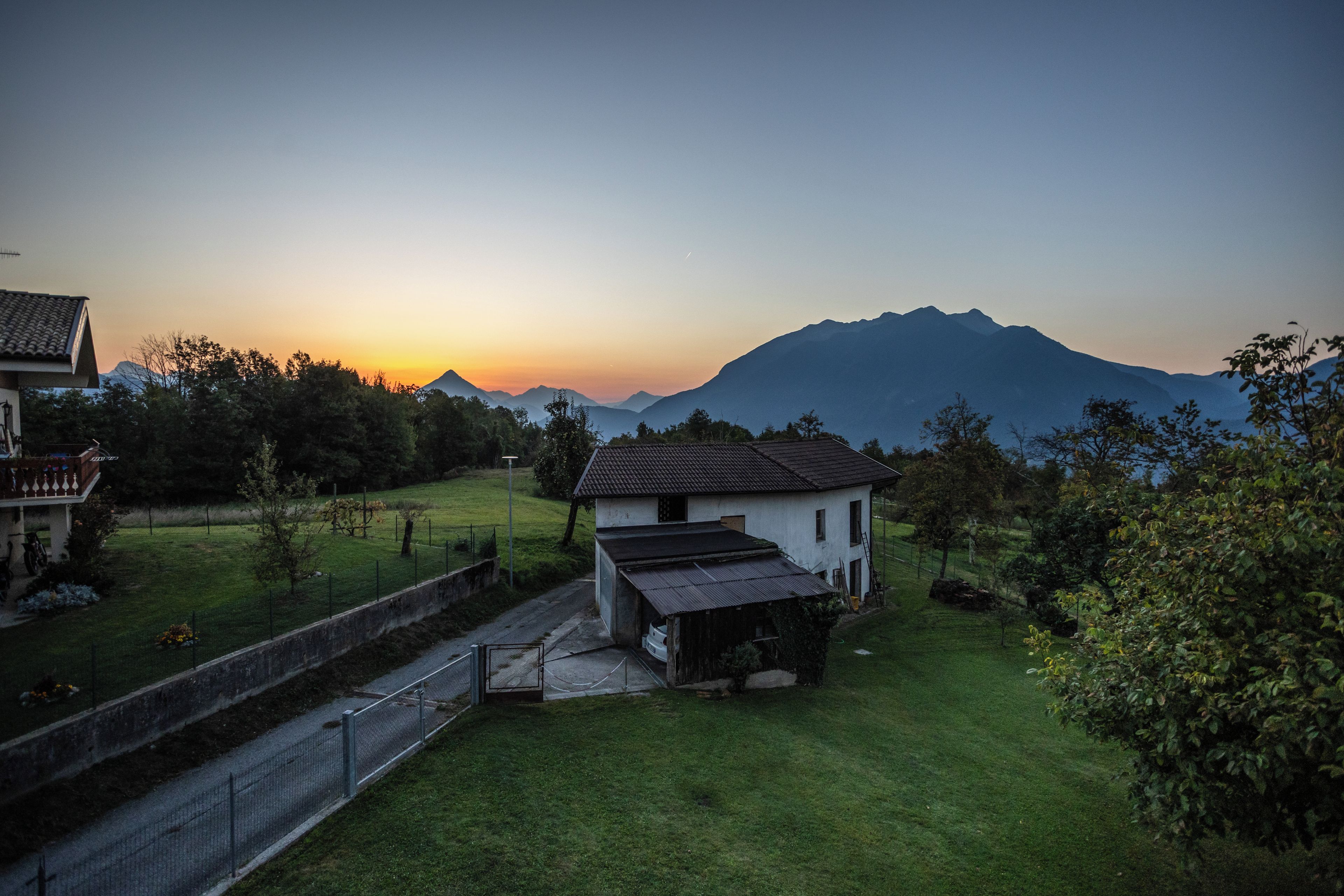 A rural landscape with a house, a small garden, and a mountain in the background.