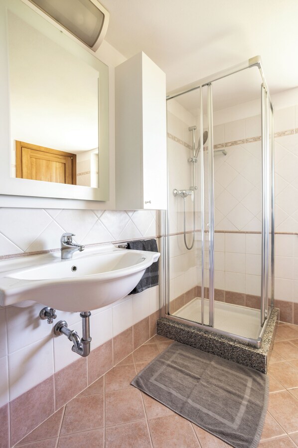 Baño con lavamanos, espejo, ducha y paredes con azulejos.