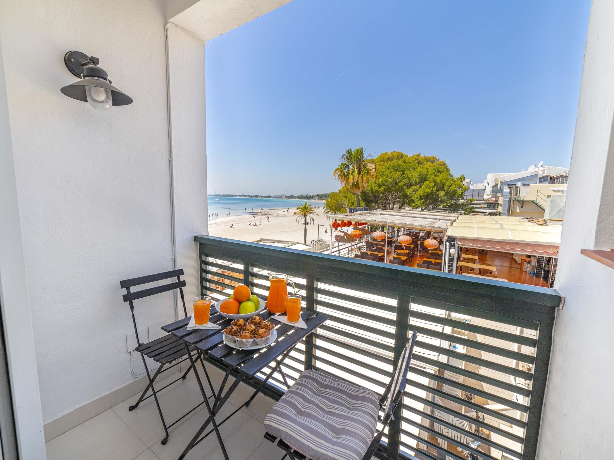 Un balcon avec une table préparée pour le petit-déjeuner, donnant sur une plage et un bâtiment équipé de panneaux solaires.