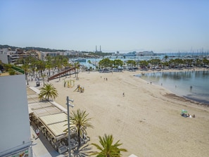 Una playa con un parque infantil, palmeras y un puerto deportivo al fondo.