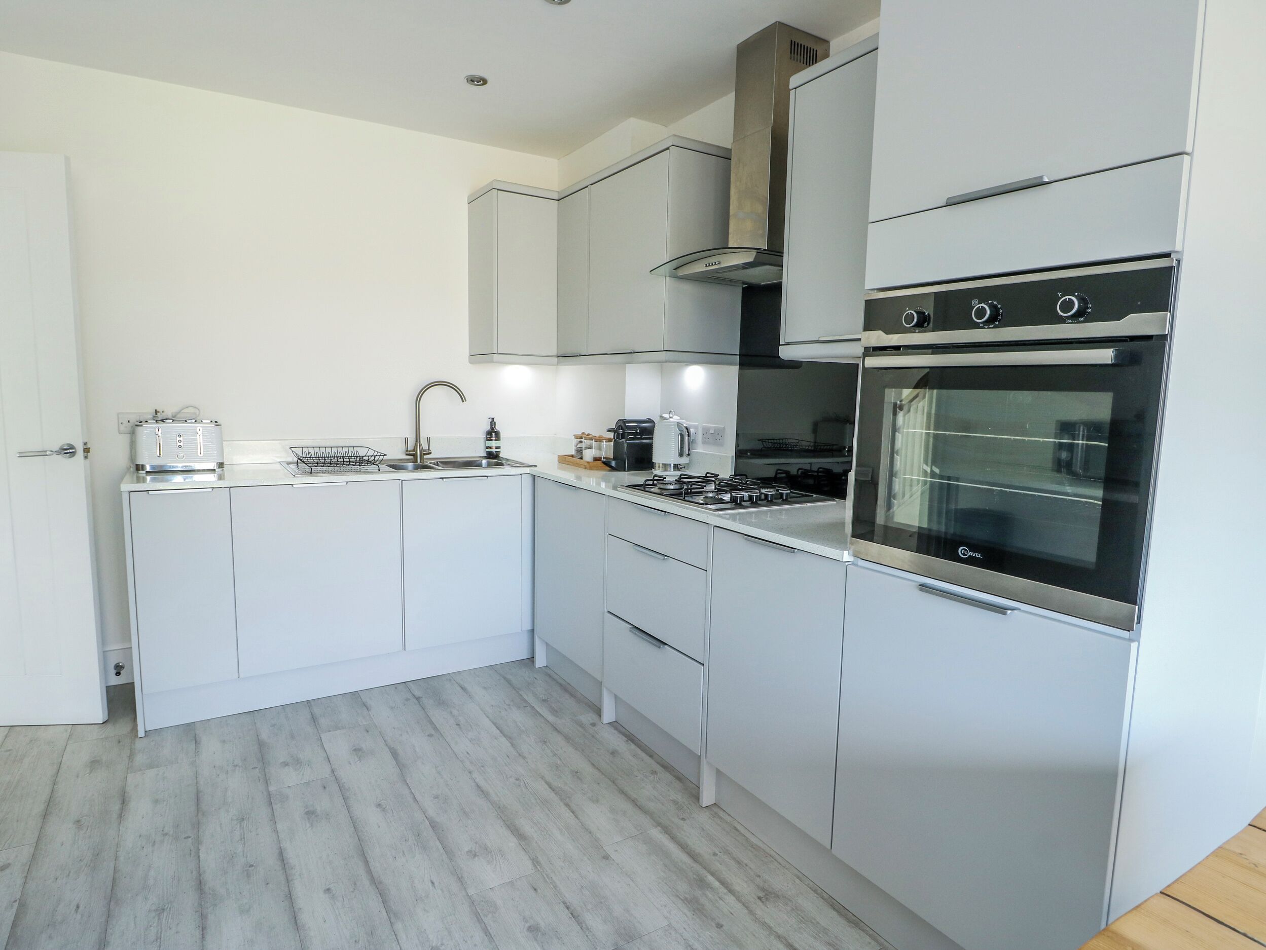 A modern kitchen with white cabinets, a stainless steel range hood, and a built-in oven.