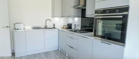 A modern kitchen with white cabinets, a stainless steel range hood, and a built-in oven.