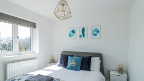 A bedroom with a bed, a window, a radiator, a bedside table, and wall art. - Dune Retreat (Ty Croes)