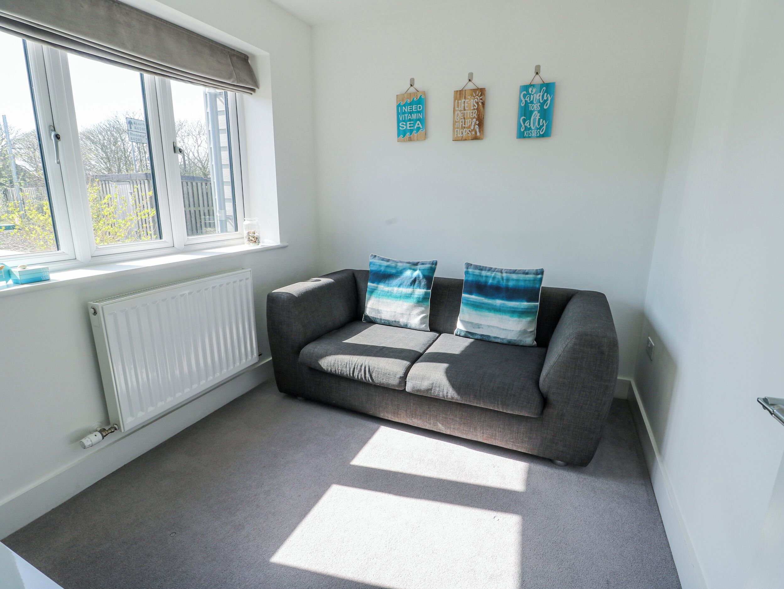 A room with a grey sofa, two blue and white patterned cushions, a white radiator, and three wall decorations.