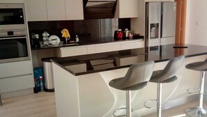 A modern kitchen with a central island, bar stools, a built-in oven, and a stainless steel refrigerator. - VILLA FOR 6 PEOPLE, POOL AND BBQ (Mioma)