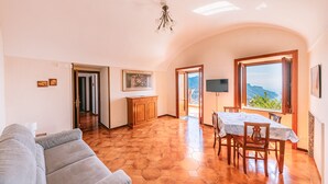 A spacious living area with a sofa, a dining table with chairs, a wooden cabinet, and a TV mounted on the wall. - Apt Anna in Villa Laura near Ravello  (scala)