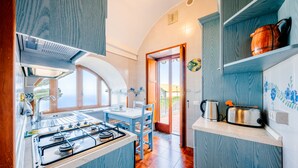 A compact kitchen with a gas stove, a toaster, and a kettle on the countertop. - Apt Anna in Villa Laura near Ravello  (scala)