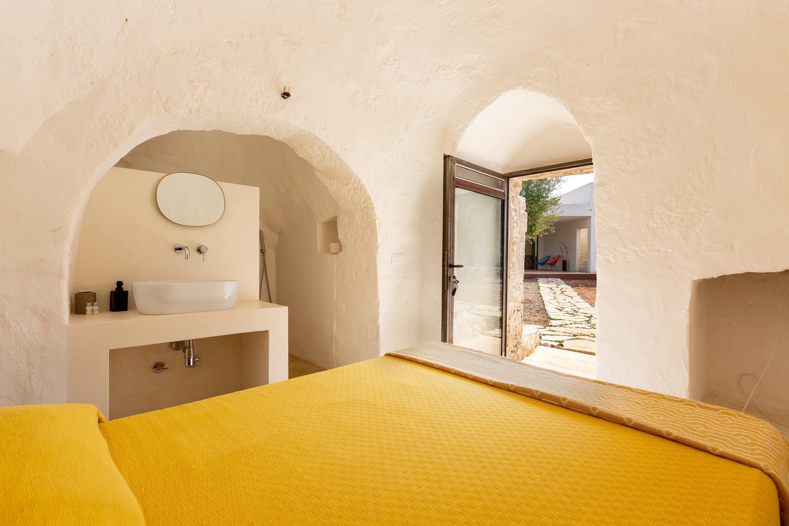 A bedroom with a bed, a sink, and a view through an arched doorway.