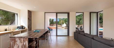 A modern kitchen with a wooden island, a dining area with chairs, and a large grey sofa.